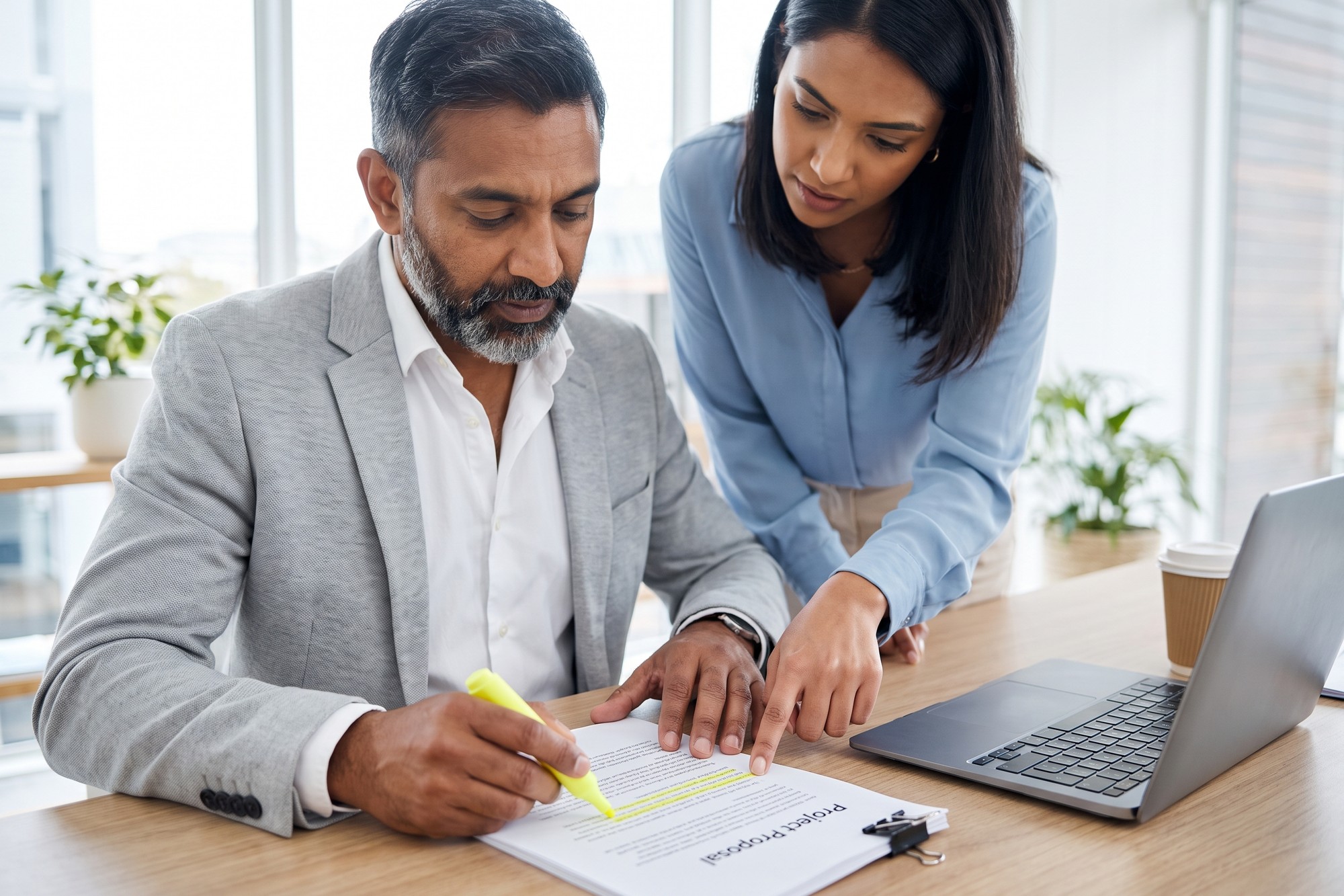 Business owner highlighting a printed project proposal on his desk while a colleague points to the same paragraph